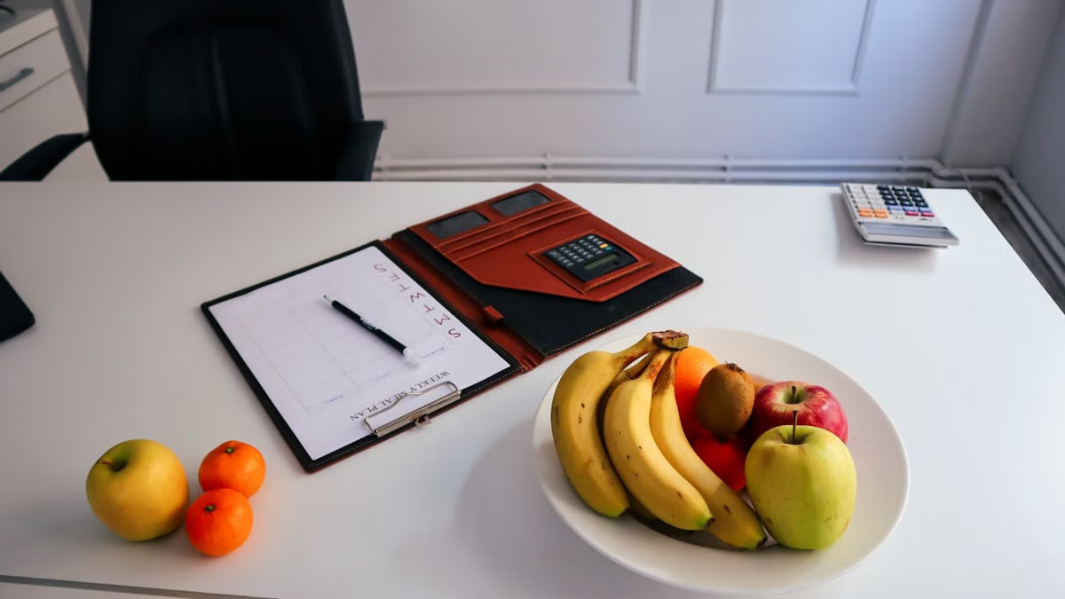 A neat office desk setup with fresh fruits, a planner, and a calculator for organized work days.